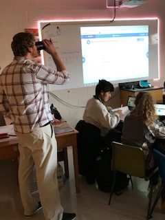 Earth Science teacher Aaron Grabinksi enjoys a sip of coffee while teaching his students work on a project. 