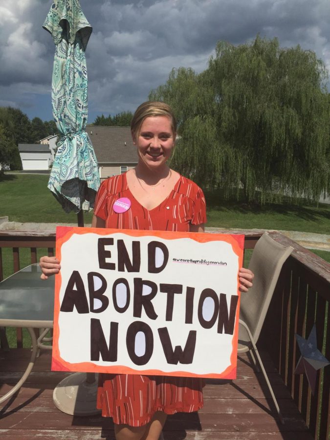 Reagan Woody holding a pro-life sign that reads  End Abortion Now. Smaller text off the the side reads #wearetheprolifegeneration. 