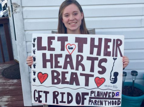 An anti-abortion sign held by Reagan Woody saying: Let their hearts beat. Get rid of Planned Parenthood. 


