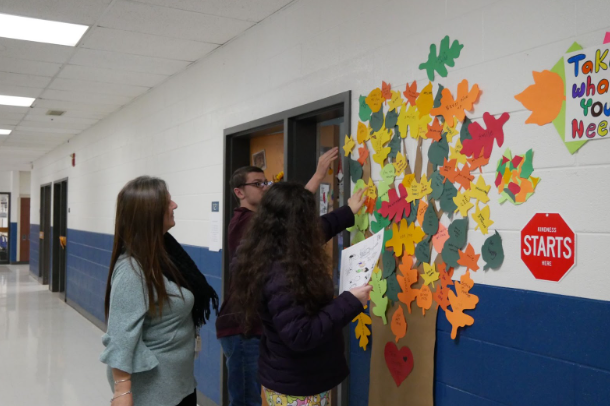 Ms. Caryn Wiley, freshman Morrighan Mackiernan, and freshman Chandler Frazier decorate The Giving Tree with leaves.