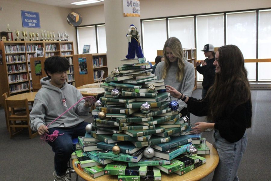 Sophomore Noah Carroll and seniors Anna Cunningham and Grace Rolon build the book tree in the library. Photo by Maxwell Pearson