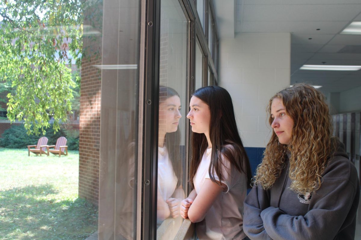 Writers, Grace Fleshman and Ella Cate Brown, look out of the hallway window into the locked courtyard.