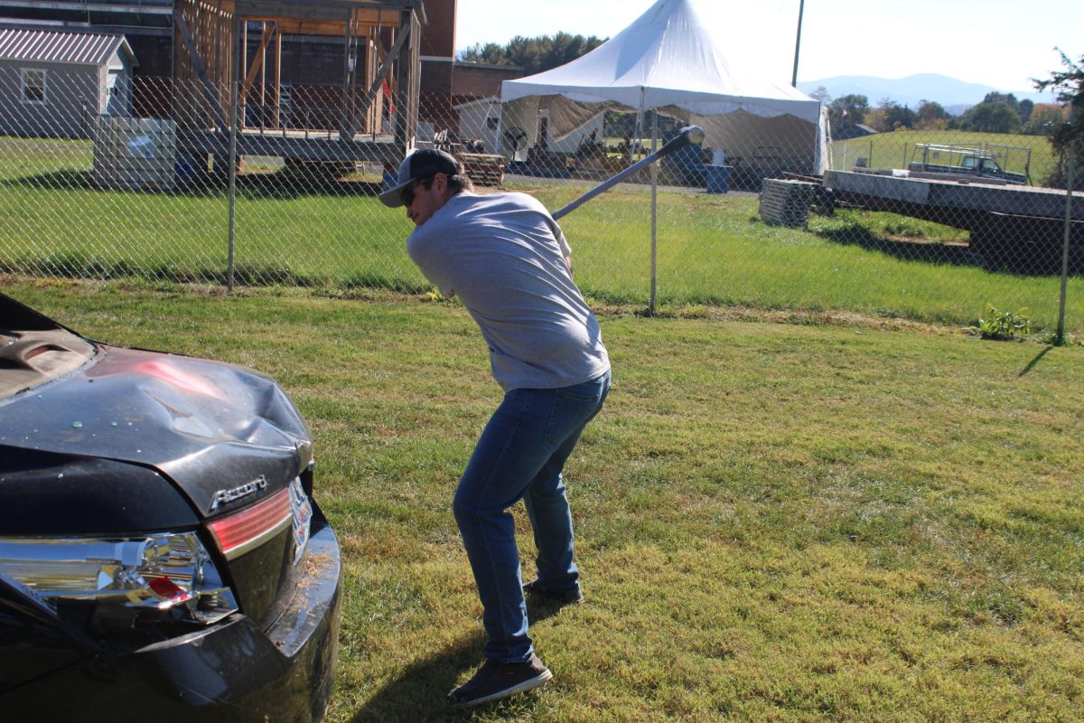 Junior Caleb Robinson hits the car with a sledgehammer.